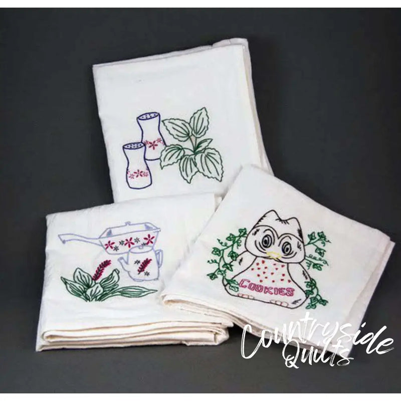 Set of embroidered white kitchen towels featuring floral and kitchenware designs from Aunt Martha’s